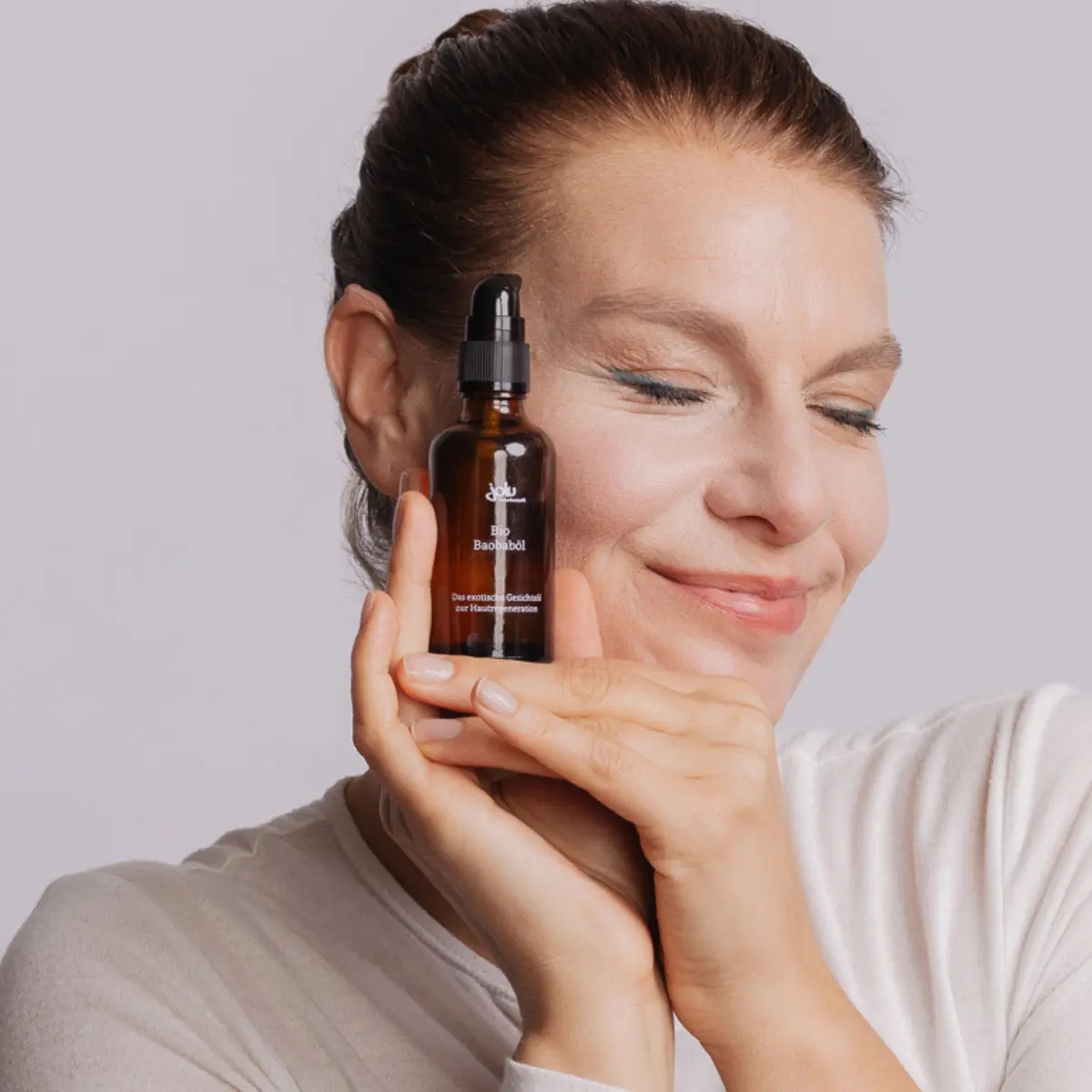 Frau trägt sanft Gesichtscreme von jolu auf ihr Gesicht auf Glasflasche Baobaböl