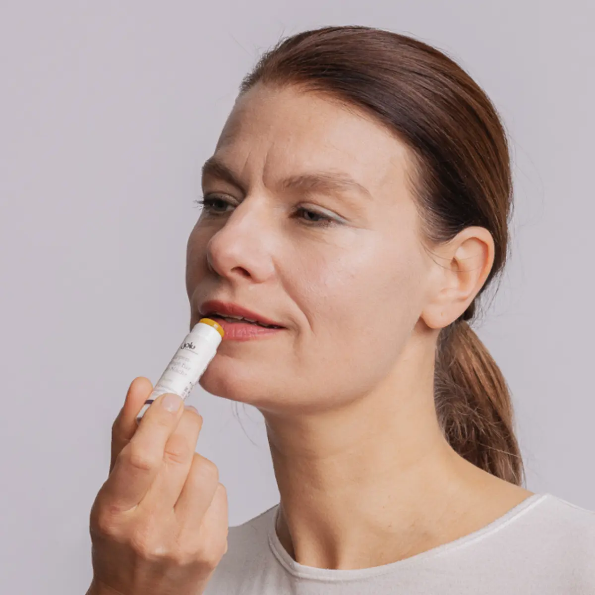 Frau trägt Lippenpflege mit einem Stick auf die Lippen auf.
