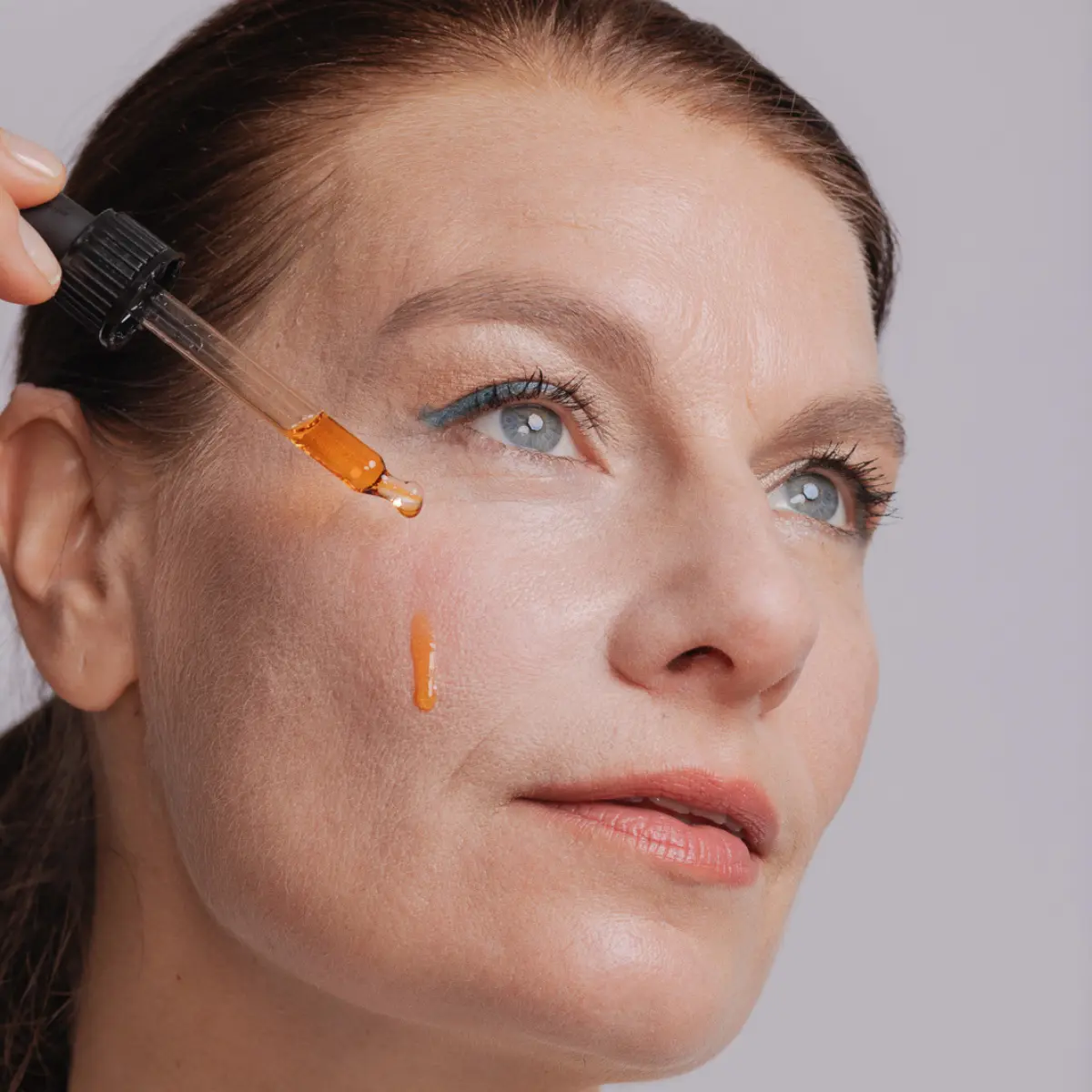 Frau trägt Bakuchiol-Serum mit einer Pipette auf ihre Wange auf.